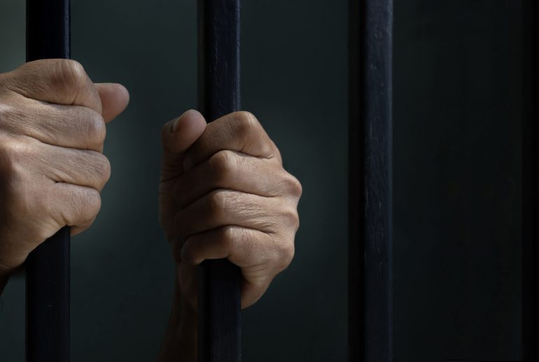 Hand of convicted prisoner behind the cell bar inside jail for incarceration, criminal and limited freedom